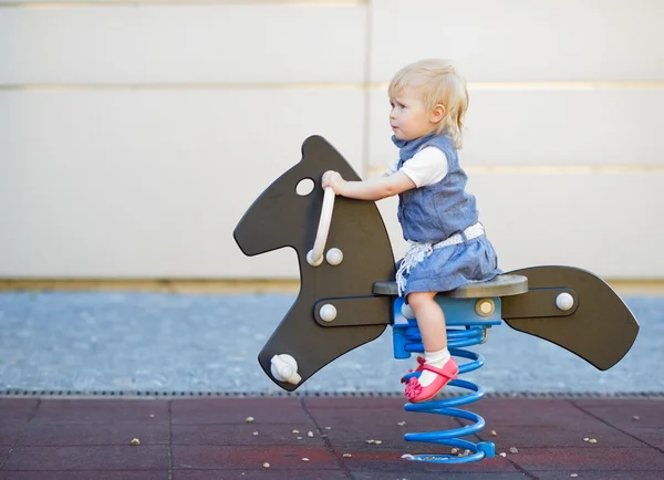 Szczęśliwe dziecko kołysanie na konia na plac zabaw dla dzieci. widok z boku — Zdjęcie stockowe