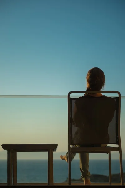 Γυναίκα απολαμβάνοντας το ηλιοβασίλεμα κάθεται στο μπαλκόνι. πίσω όψη — Φωτογραφία Αρχείου
