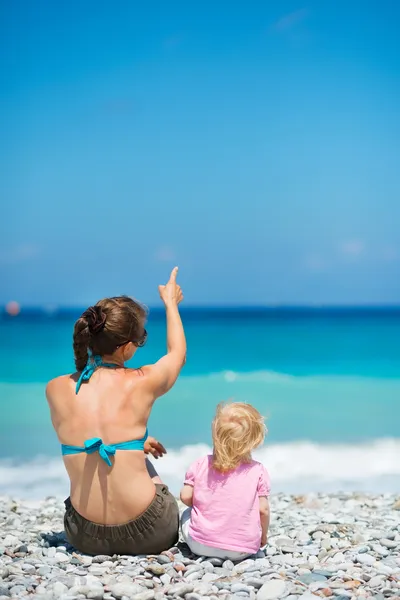 Mãe sentada com o bebê na praia e apontando no espaço de cópia. Re — Fotografia de Stock