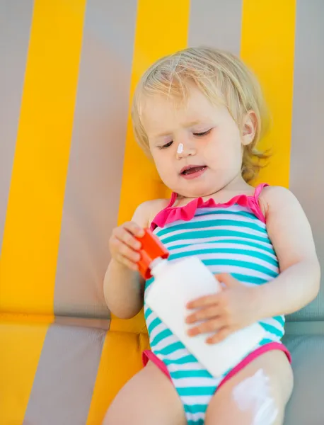 Bambino sdraiato sul lettino con bottiglia di crema solare — Foto Stock