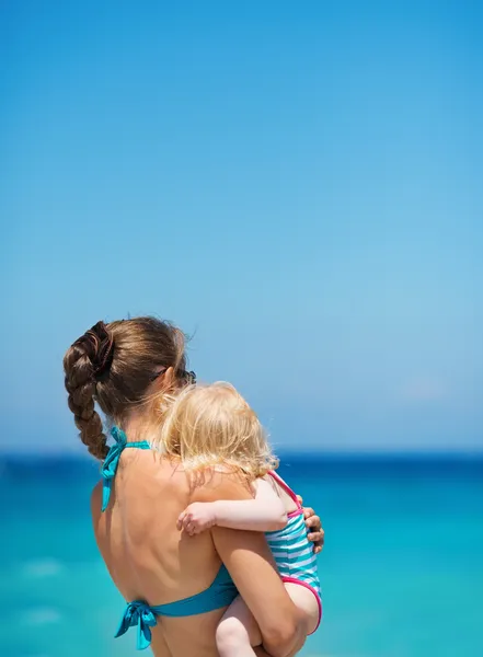 Μητέρα με το μωρό στην ακτή της θάλασσας που ψάχνει σε απόσταση. πίσω όψη — Φωτογραφία Αρχείου