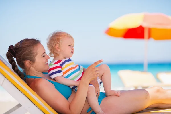 Mother with baby laying on sunbed and pointing on copy space — Stock Photo, Image