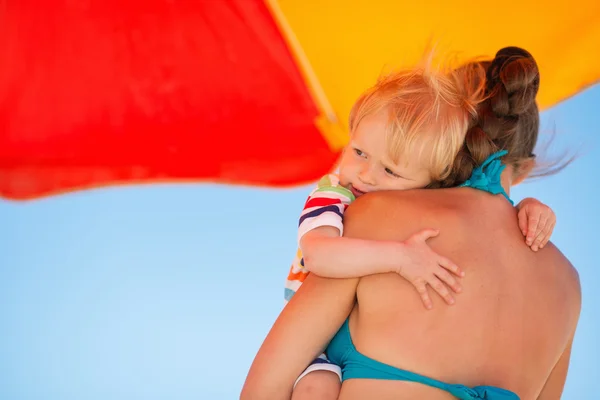 Ребенок обнимает мать на пляже под зонтиком — стоковое фото