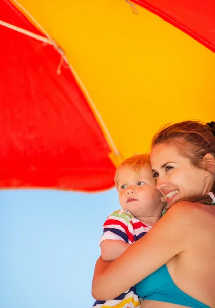 Matka i dziecko patrząc na miejsce na plaży pod parasolem — Zdjęcie stockowe
