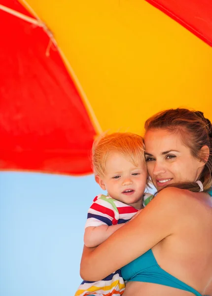 Portret van moeder en baby op strand onder de paraplu — Stockfoto