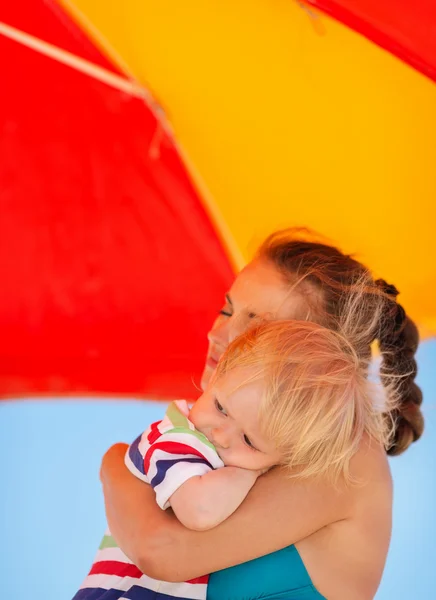 Mutter umarmt Baby am Strand unter Sonnenschirm — Stockfoto