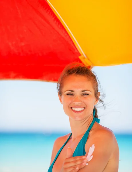 Femme souriante appliquant crème solaire sur le bras — Photo