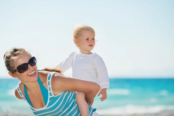 Baby on beach piggybacking mother and looking on copy space — Stock Photo, Image