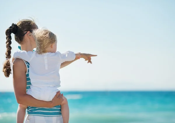 Mother and baby on beach pointing on copy space — Stock Photo, Image