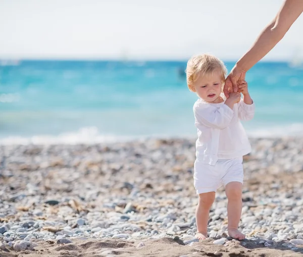 Baby holding mothers hand and walking on beach — Stock Photo, Image
