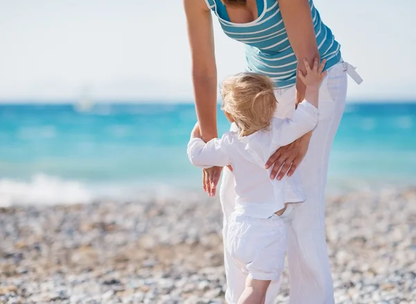 Baby on beach climbing mothers hands — Stock Photo, Image