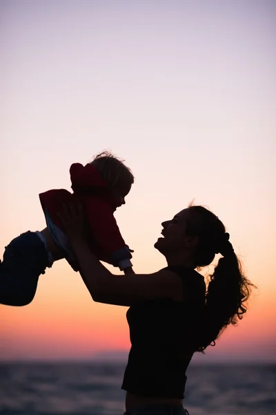 Silhuett av mamma leker med baby i solnedgången — Stockfoto