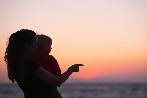 Silhouette af mor med baby i solnedgang peger på kopiplads - Stock-foto