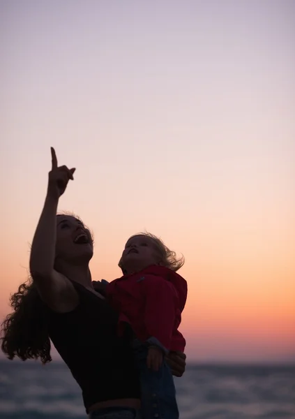 Silhouette of mother with baby in dusk pointing up on copy space — Stock Photo, Image