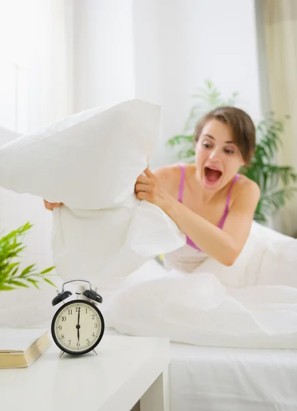 Stock image Angry woman trying to break alarm clock by pillow