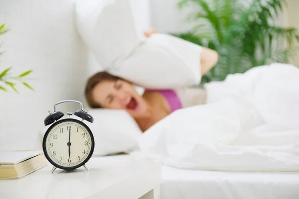 Mujer molesta cerrando oídos por almohada para evitar oír despertador —  Fotos de Stock