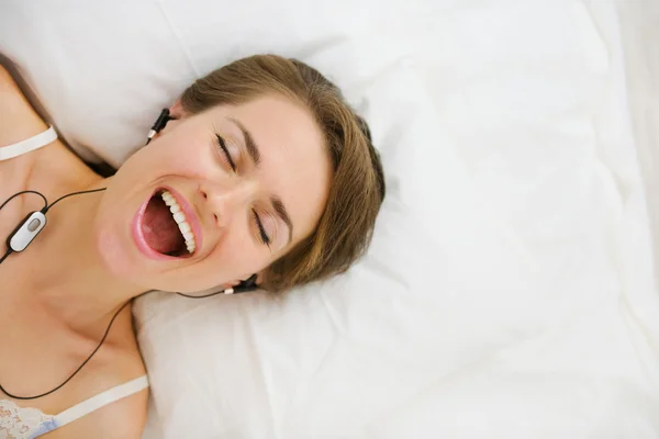Портрет девушки в наушниках, лежащей на кровати и слушающей музыку — стоковое фото