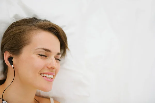 Портрет лежащей на кровати девушки в наушниках слушающей музыку. Вверх — стоковое фото