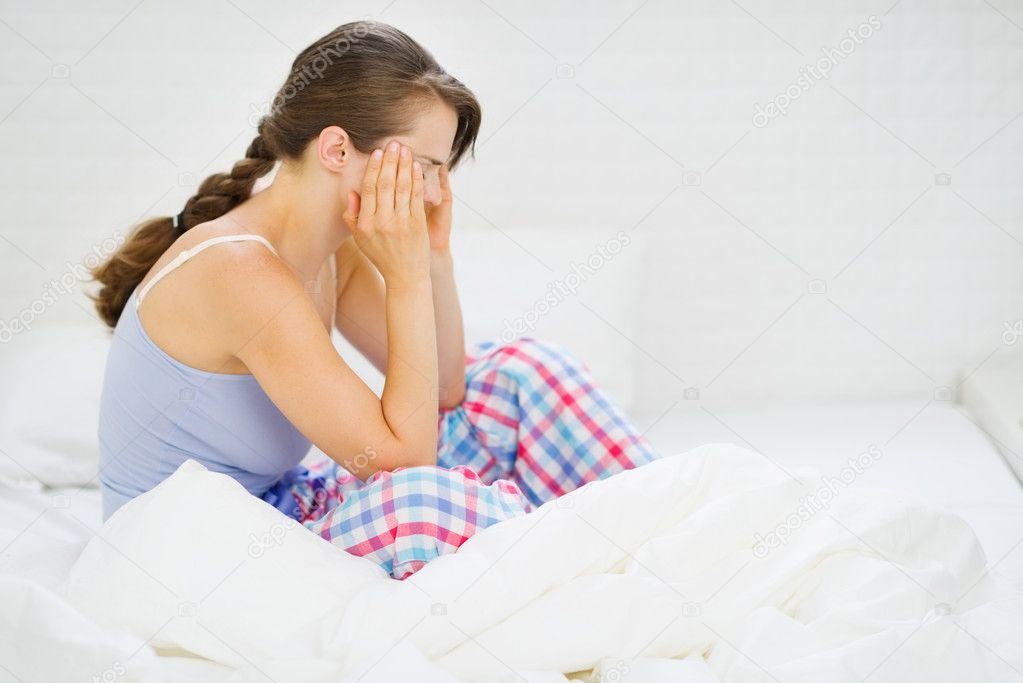 Woman with head ache sitting on bed