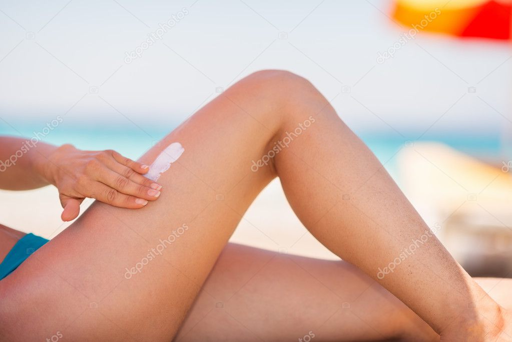 Closeup on female hand applying sun block creme on leg