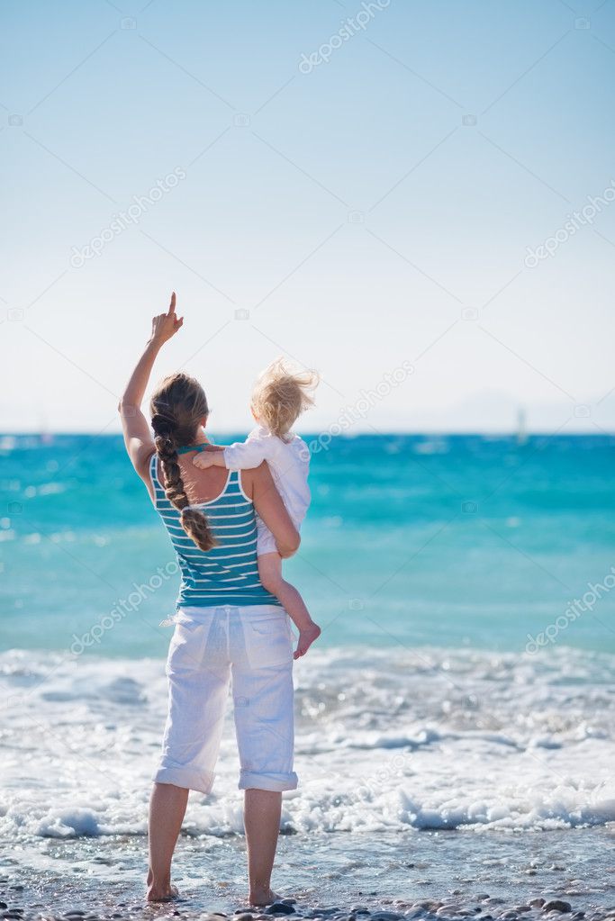 Mother and baby on sea coast pointing on copy space