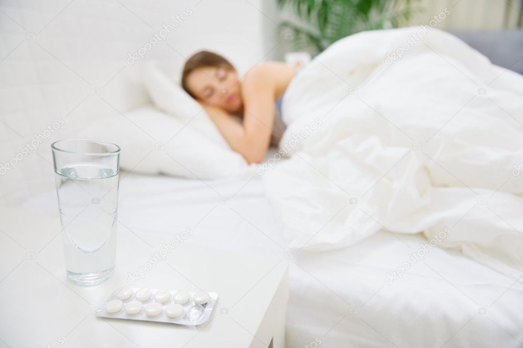 Glass of water and pack of pills on table and woman sleeping in