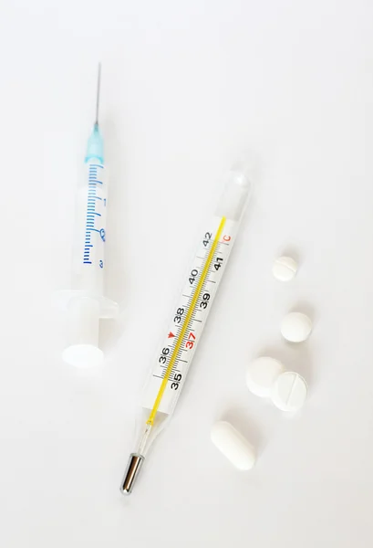Termómetro clínico, jeringa y pastillas blancas —  Fotos de Stock