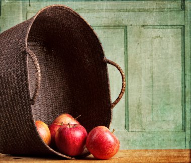 Apples spilling out of basket on grunge background clipart