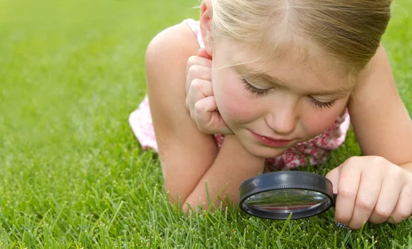 Girl looking through magnifying glass outdoors — Stock Photo, Image