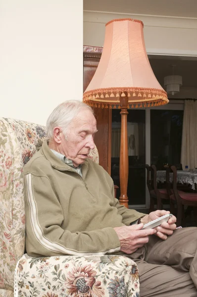 Ηλικιωμένος άνδρας κάθεται σε μια πολυθρόνα χρησιμοποιώντας το τηλεχειριστήριο της τηλεόρασης — Φωτογραφία Αρχείου