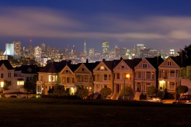 Night descends on the iconic Painted Ladies row of Victorian houses backed by downtown San Francisco during blue hour in California clipart