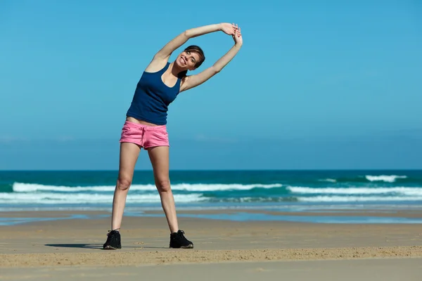 Fitness tjej stretching på stranden — Stockfoto