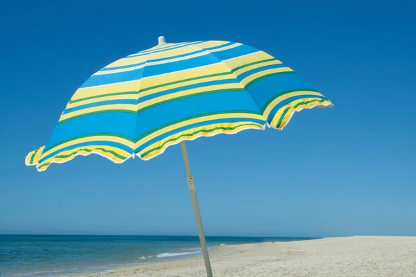 Kumlu bir plaj üzerinde mavi ve sarı şemsiye — Stok fotoğraf