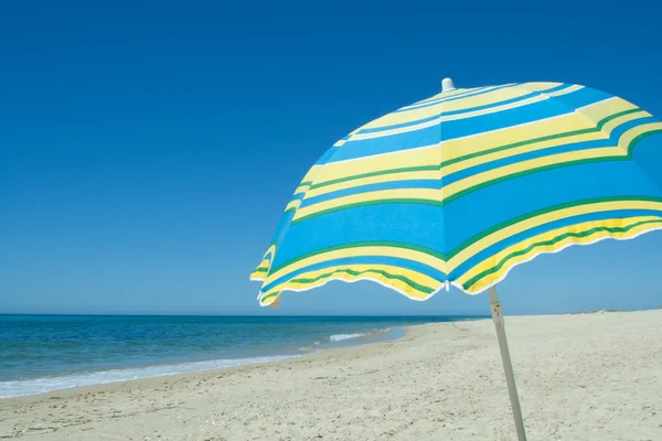 Kumlu bir plaj üzerinde mavi ve sarı şemsiye — Stok fotoğraf