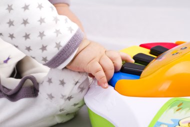 Newborn baby boy playing with a toy piano clipart