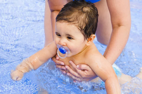 Новорожденный ребенок с пустышкой играет в бассейне со своей матерью — стоковое фото