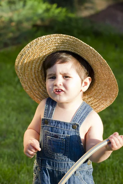 Мальчик в соломенной шляпе, молодой аутфилдер, играющий со шлангом — стоковое фото