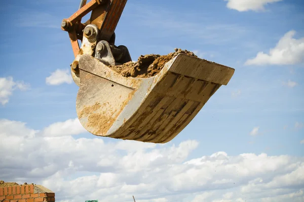 Excavator standing in sandpit with raised bucket over cloudscape Stock Image