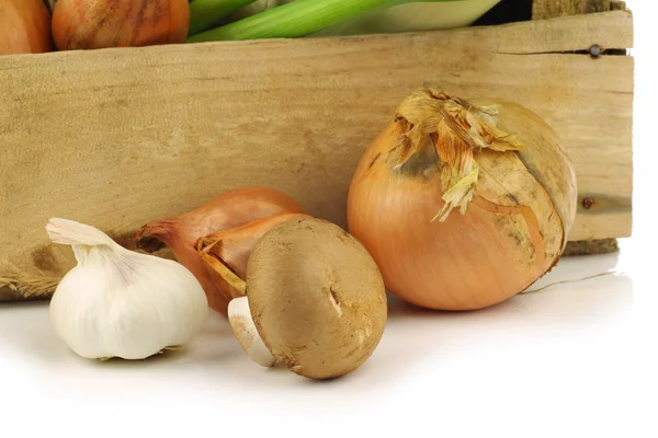 Frische Zwiebeln, Knoblauch und Pilze vor einer Holzkiste — Stockfoto
