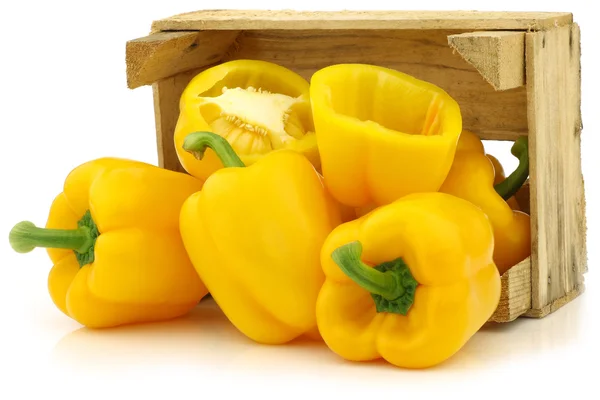 Fresh yellow bell peppers (capsicum) and a cut one in a wooden crate — Stock Photo, Image