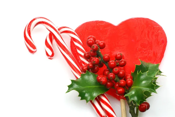 Christmas candy canes with a branch of holly on a red hart — Stock Photo, Image