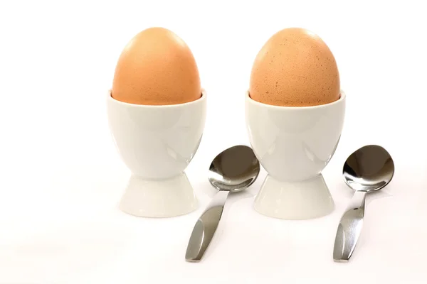 Two white egg cups with brown eggs and spoons — Stock Photo, Image