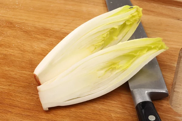 Freshly cut chicory halves and a knife on a cutting board — Stock Photo, Image
