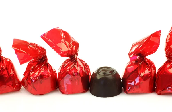 Řada bonbony v červené lesklé papíru a jeden rozbalila — Stock fotografie