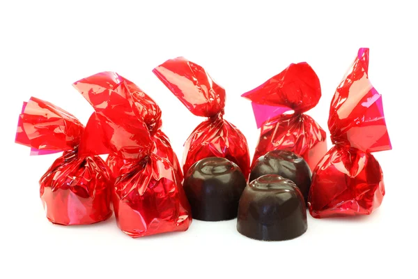 Een rij van bonbons verpakt in rood glanzend papier en drie onverpakt klaar om te eten — Stockfoto