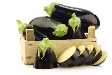 Fresh aubergines and a cut one in a wooden crate clipart