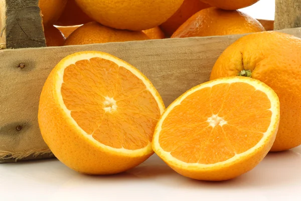 Čerstvé pomeranče a dvě půlky v dřevěné krabici — Stock fotografie