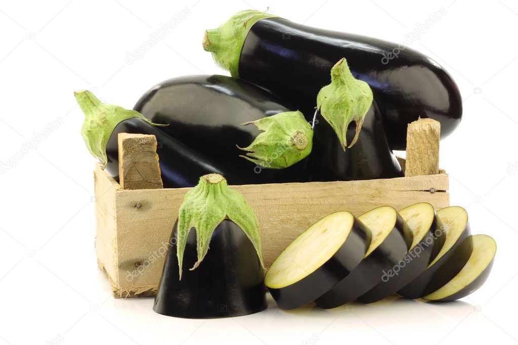 Fresh aubergines and a cut one in a wooden crate