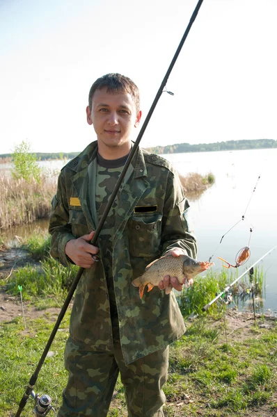 Pescador sosteniendo carpas en la orilla del río —  Fotos de Stock