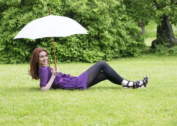 Young woman with umbrella lying in a park — Stock Photo, Image
